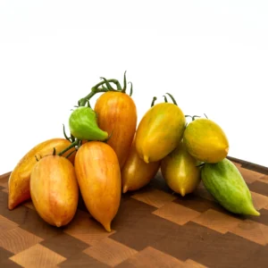 Dream Cream heirloom tomatoes, mostly orange with touches of green and yellow, are arranged on a wooden cutting board against a plain white background.