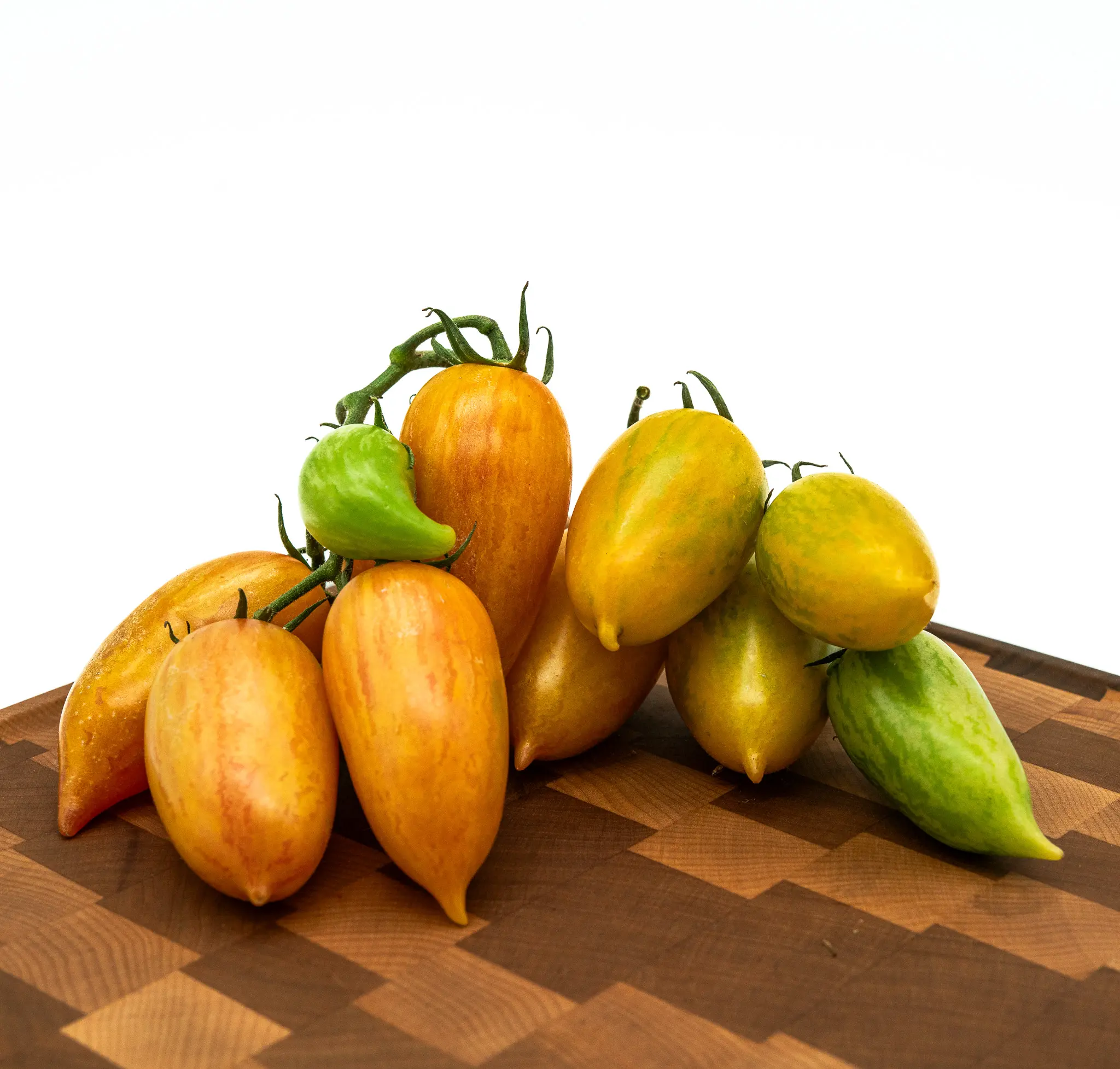 Dream Cream heirloom tomatoes, mostly orange with touches of green and yellow, are arranged on a wooden cutting board against a plain white background.